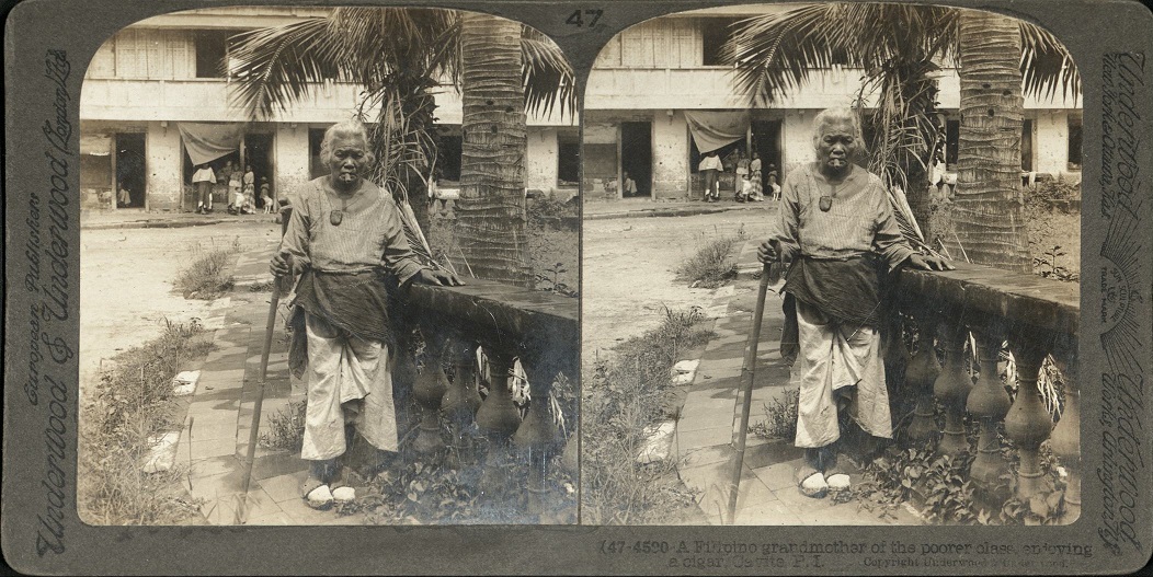 A Filipino grandmother of the poorer class, enjoying a cigar, Cavite, P. I.
